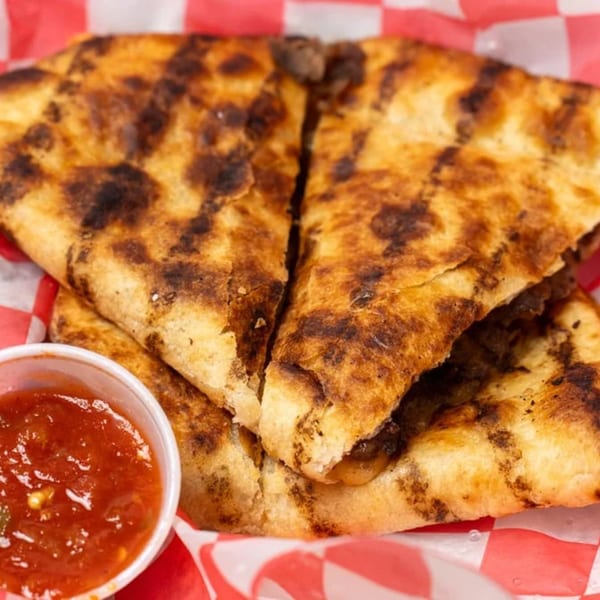 Two grilled quesadilla halves with melted cheese and meat, served with a side of salsa.