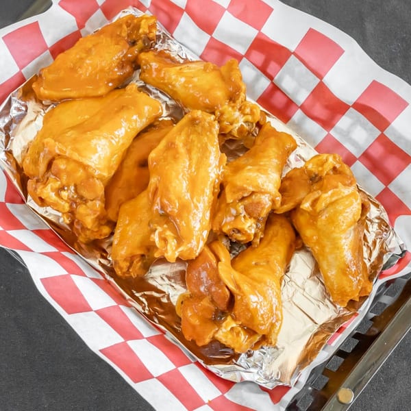 A basket of Station Pizza II's golden-brown chicken wings, coated in a savory sauce, on checkered paper.