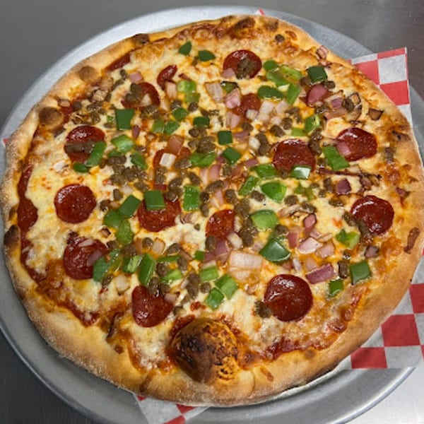 A Station Pizza II pizza with pepperoni, sausage, green peppers, and onions on a metal tray.