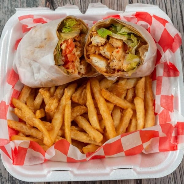 A chicken wrap cut in half with lettuce and tomatoes, served with a side of golden french fries.