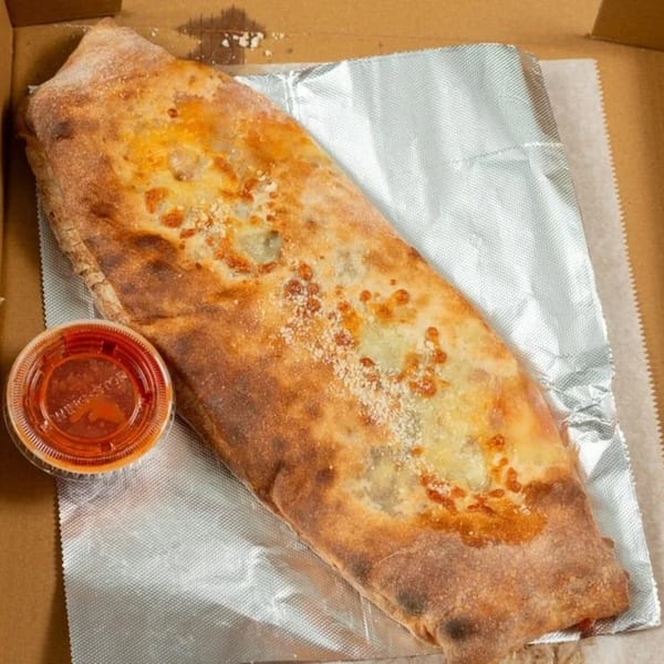 A golden-brown calzone with melted cheese and a side of marinara sauce in a takeout box.